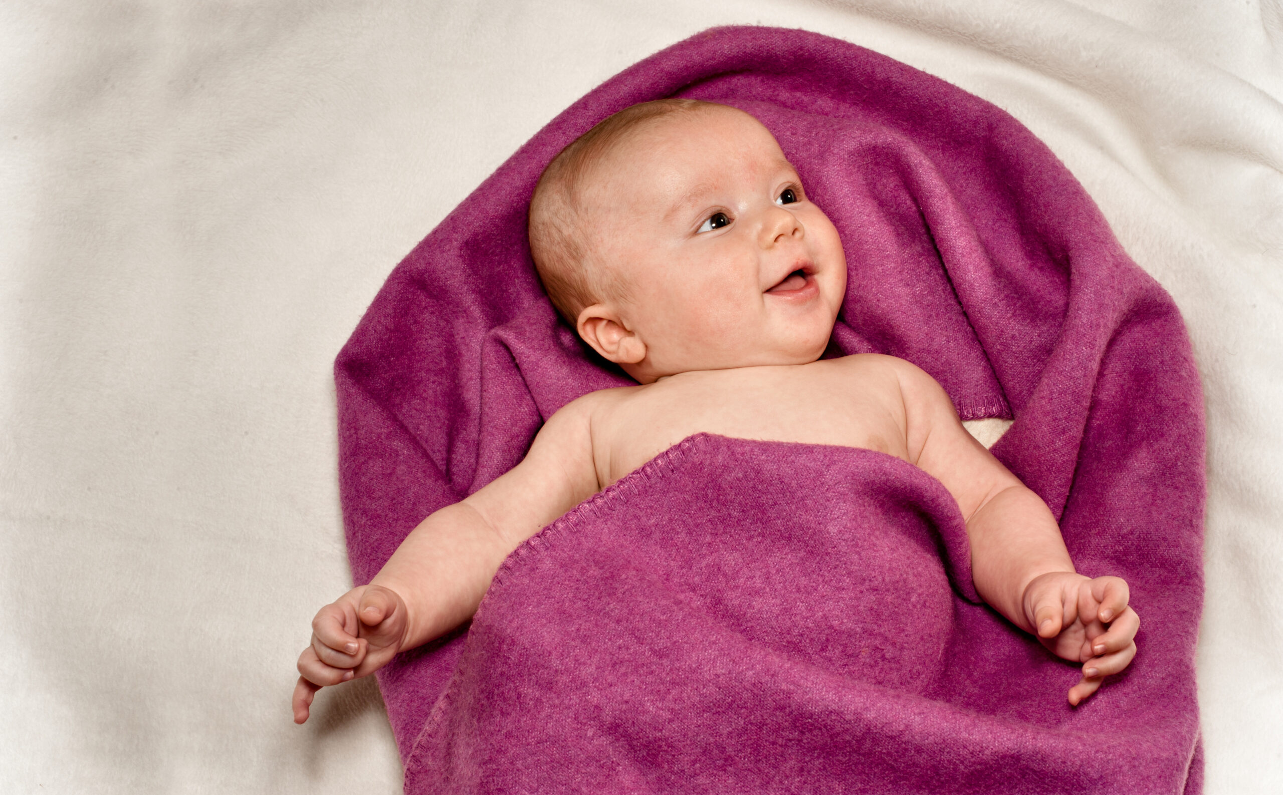 Ein Baby liegt auf einer weichen Decke und schaut aufmerksam nach oben.